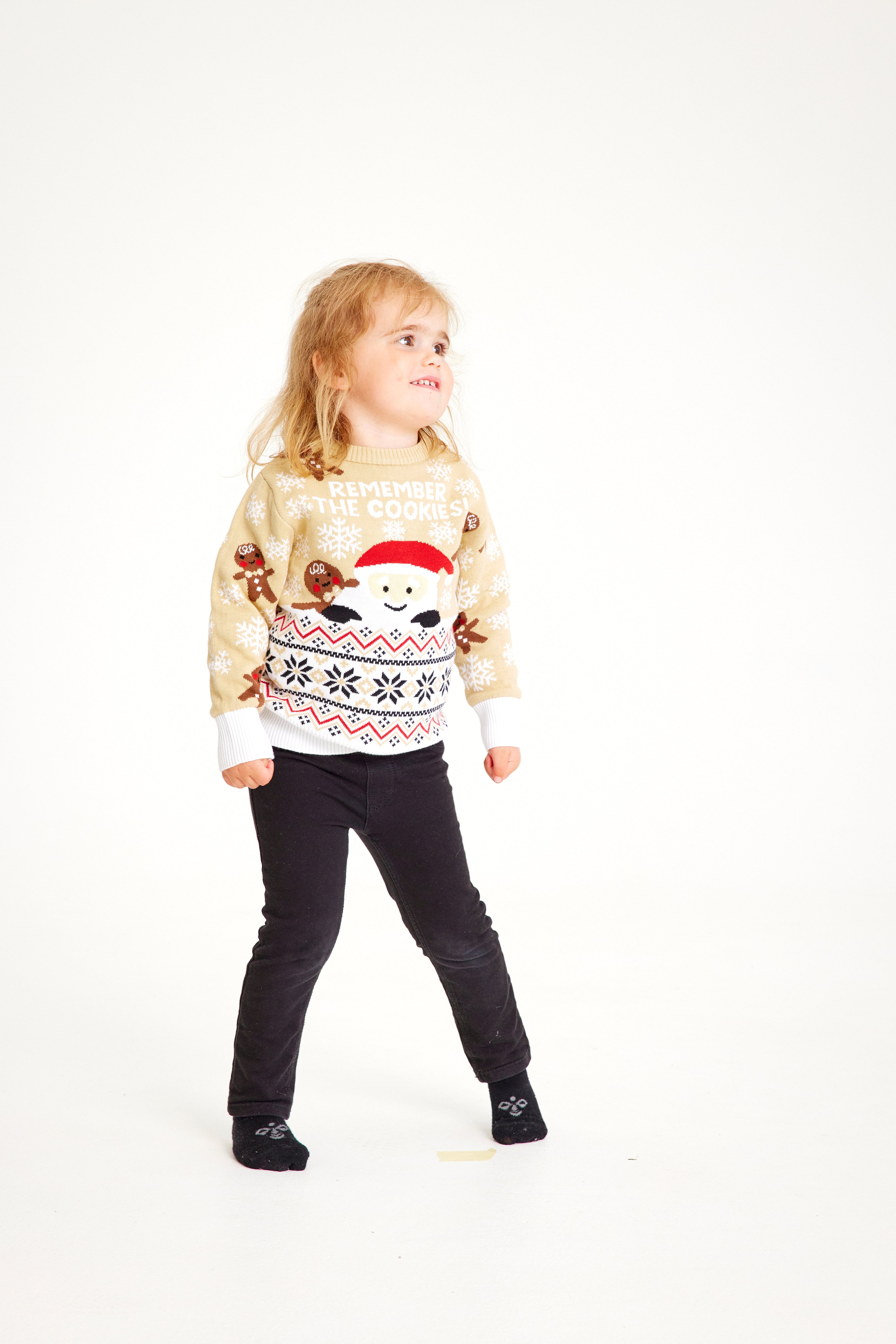 Ein Kind schaut zur Seite und trägt einen beigen Weihnachtspulli mit dem Spruch